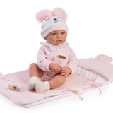 A baby doll seated on a pink bunny-shaped blanket with a matching pink and white hooded hat featuring ear pom-poms and a bear face, against a plain white background.