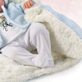 A close-up of a baby wearing white footed pajamas and being covered with a soft light blue and white blanket.
