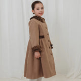 Young girl wearing a long brown coat against a white background