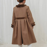Person wearing a long brown coat with ruffled details on a white background
